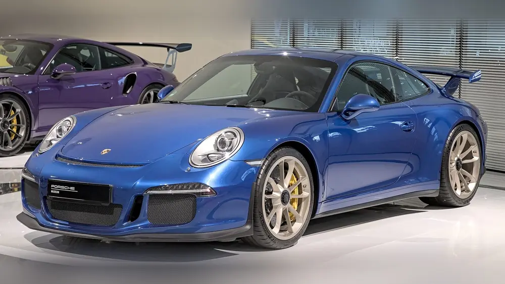 Blue Porsche 991.1 GT3 with gold wheels and a fixed rear wing, front three-quarter view, on display at the Porsche Museum