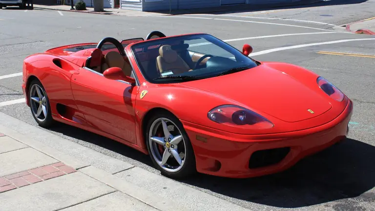 Red Ferrari 360 Spider with the top down and tan seats, front three-quarter view, parked on a small-town street