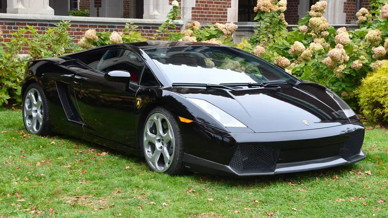 Black 2006 Lamborghini Gallardo coupe, front three-quarter view, parked on a lawn in front of a brick building