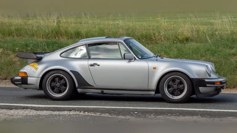 Silver Porsche 930 Turbo with its whale-tail rear spoiler, side view on a country road