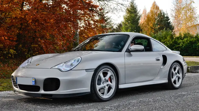 Silver Porsche 996 Turbo coupe, front three-quarter view, parked in front of autumn trees